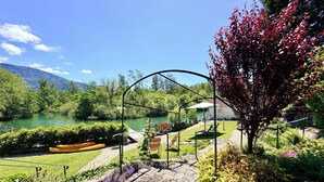 A riverside garden with a stone pathway, a metal archway, and a view of a river and mountains.