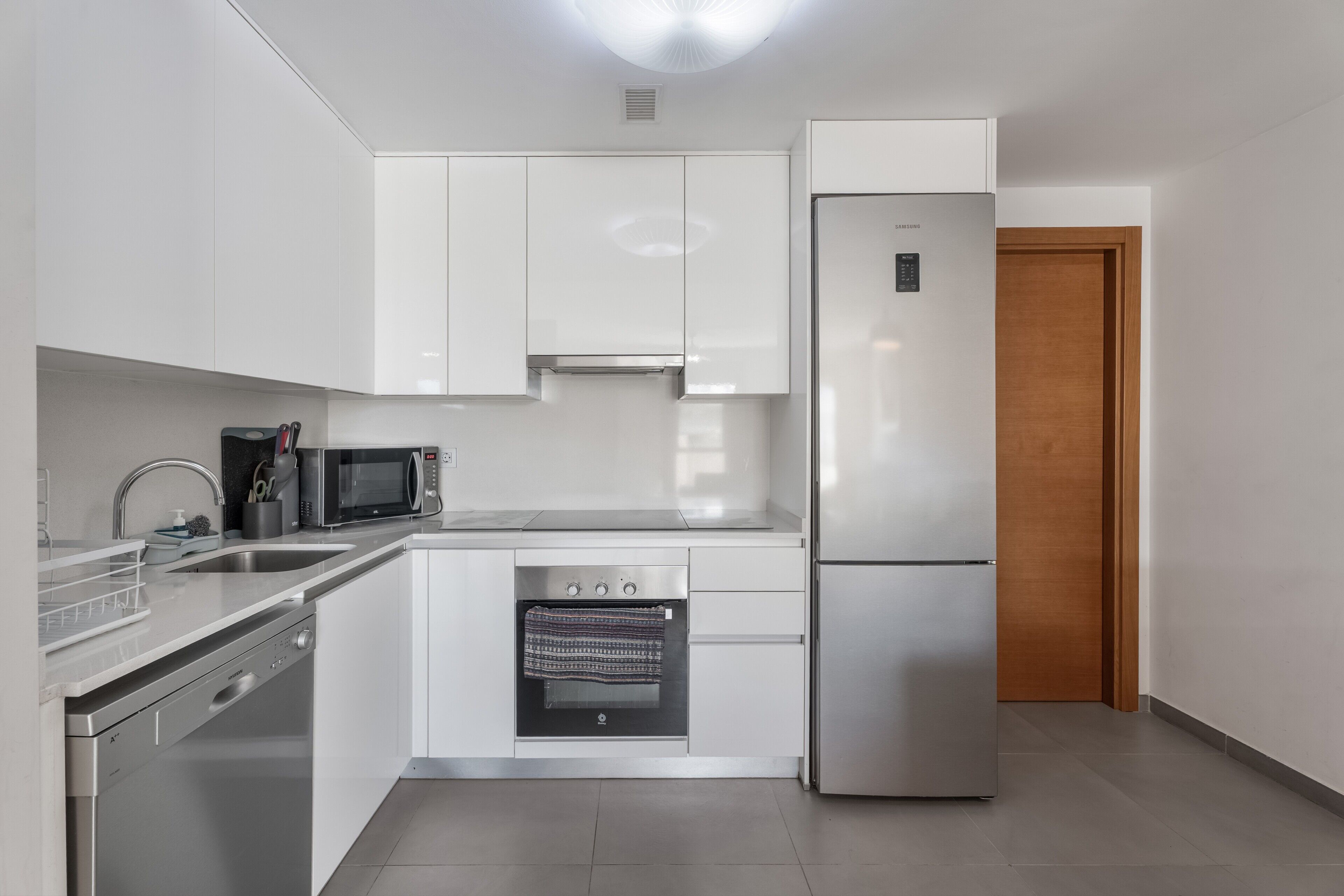 Une cuisine moderne avec des meubles blancs, des appareils en acier inoxydable, un lave-vaisselle et un four à micro-ondes.