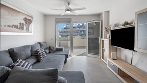 A modern living room with a grey sofa set, a flat-screen TV, and a ceiling fan.