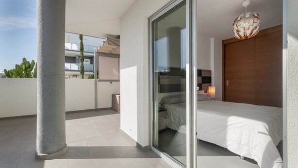 A modern bedroom with a large bed, a sliding glass door to a balcony, and a minimalist design.