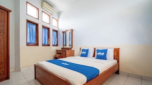 Una cama bien hecha con colcha azul y blanca, cabecera de madera y dos almohadas con la palabra "rehat".