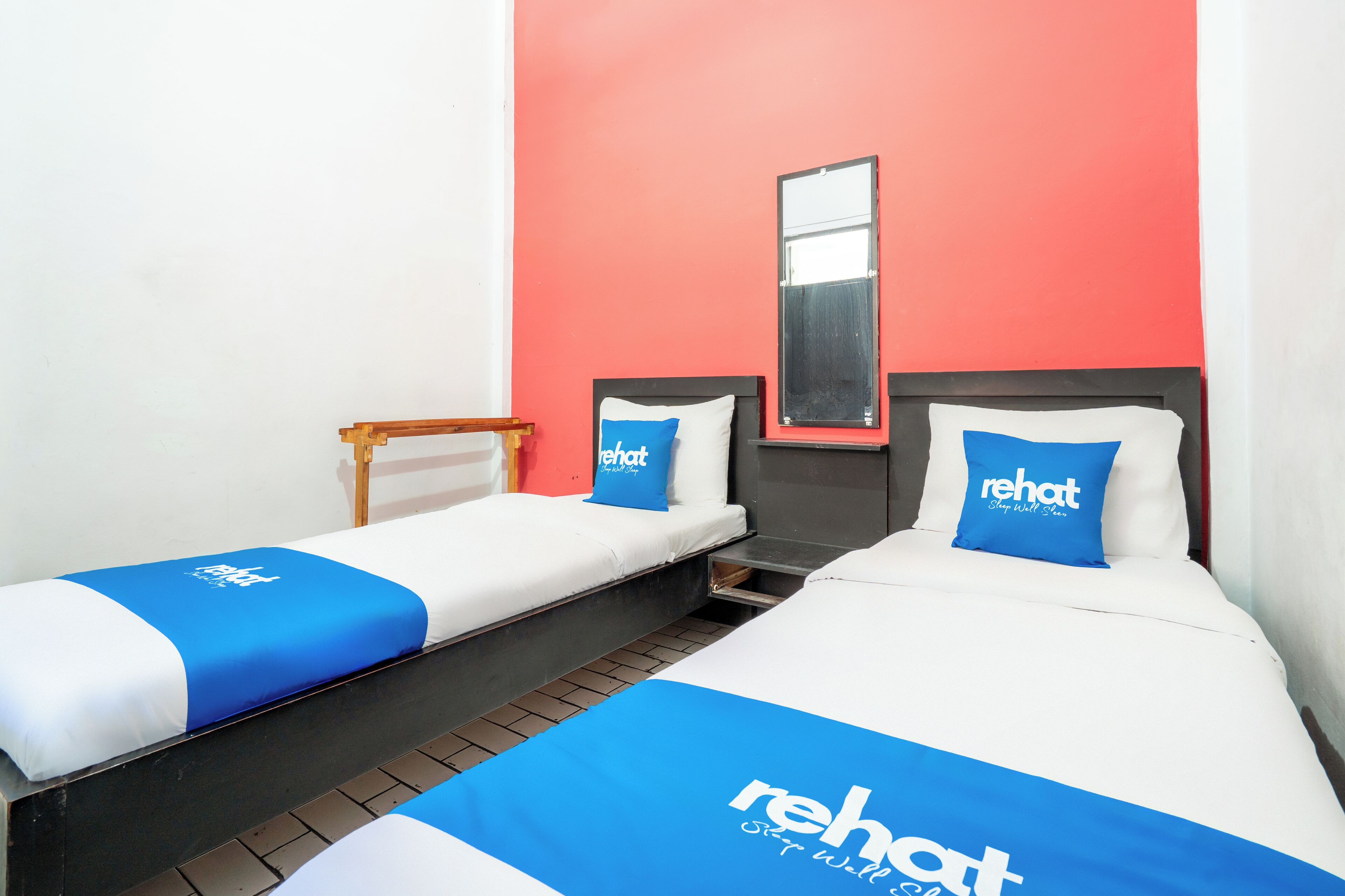 Une chambre d’hôtel avec deux lits, chacun recouvert d’une couvre-lit bleue et blanche et agrémenté d’oreillers, et un mur d’accent rouge.