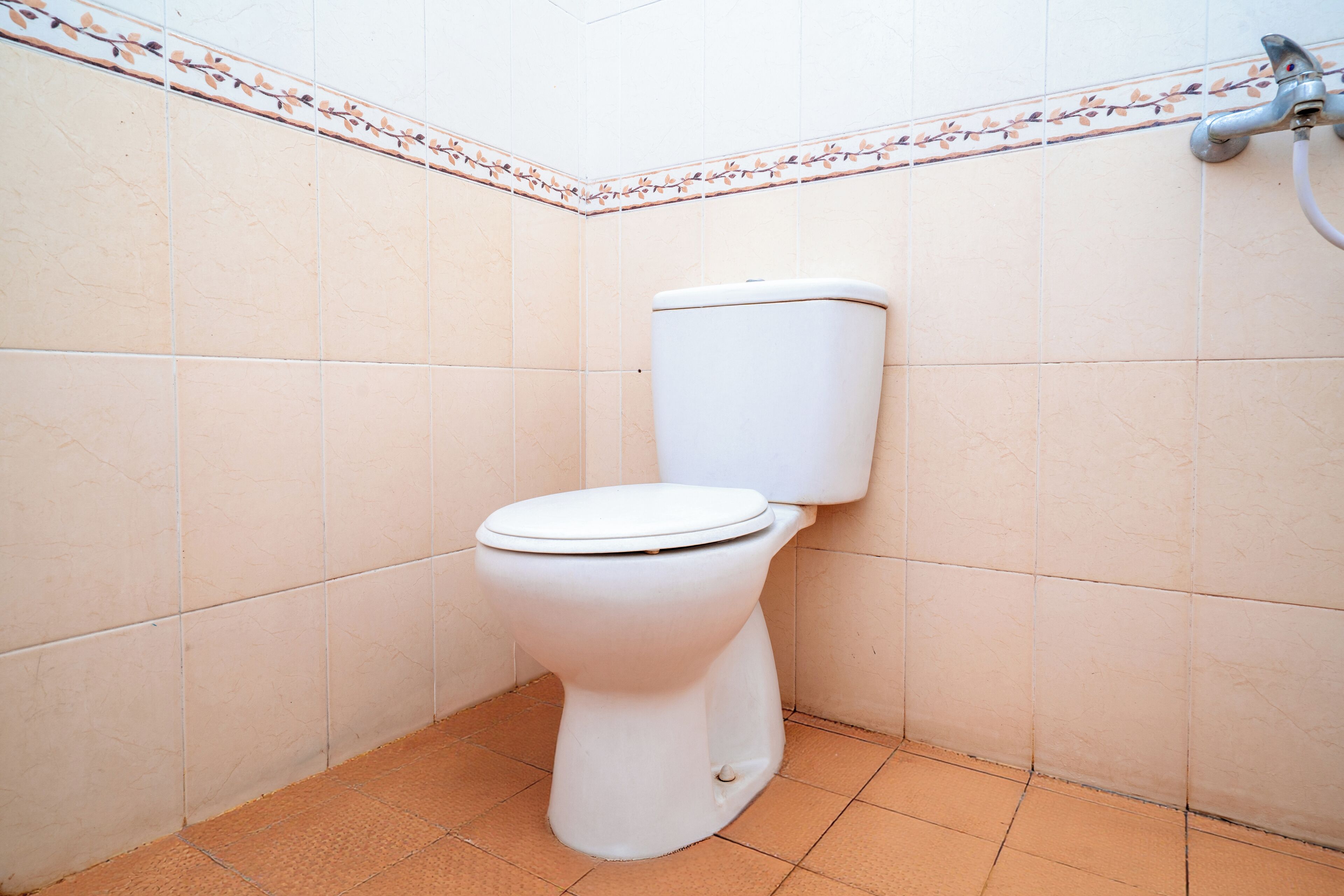 A standard white toilet in a corner of a bathroom with tiled walls and floor.