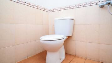 A standard white toilet in a corner of a bathroom with tiled walls and floor.