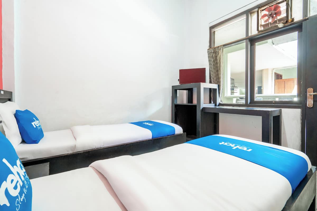 Ett hotellrum med två sängar, var och en med ett blått och vitt sängöverkast, en röd bok på ett nattduksbord och ett fönster med utsikt över omgivningen.