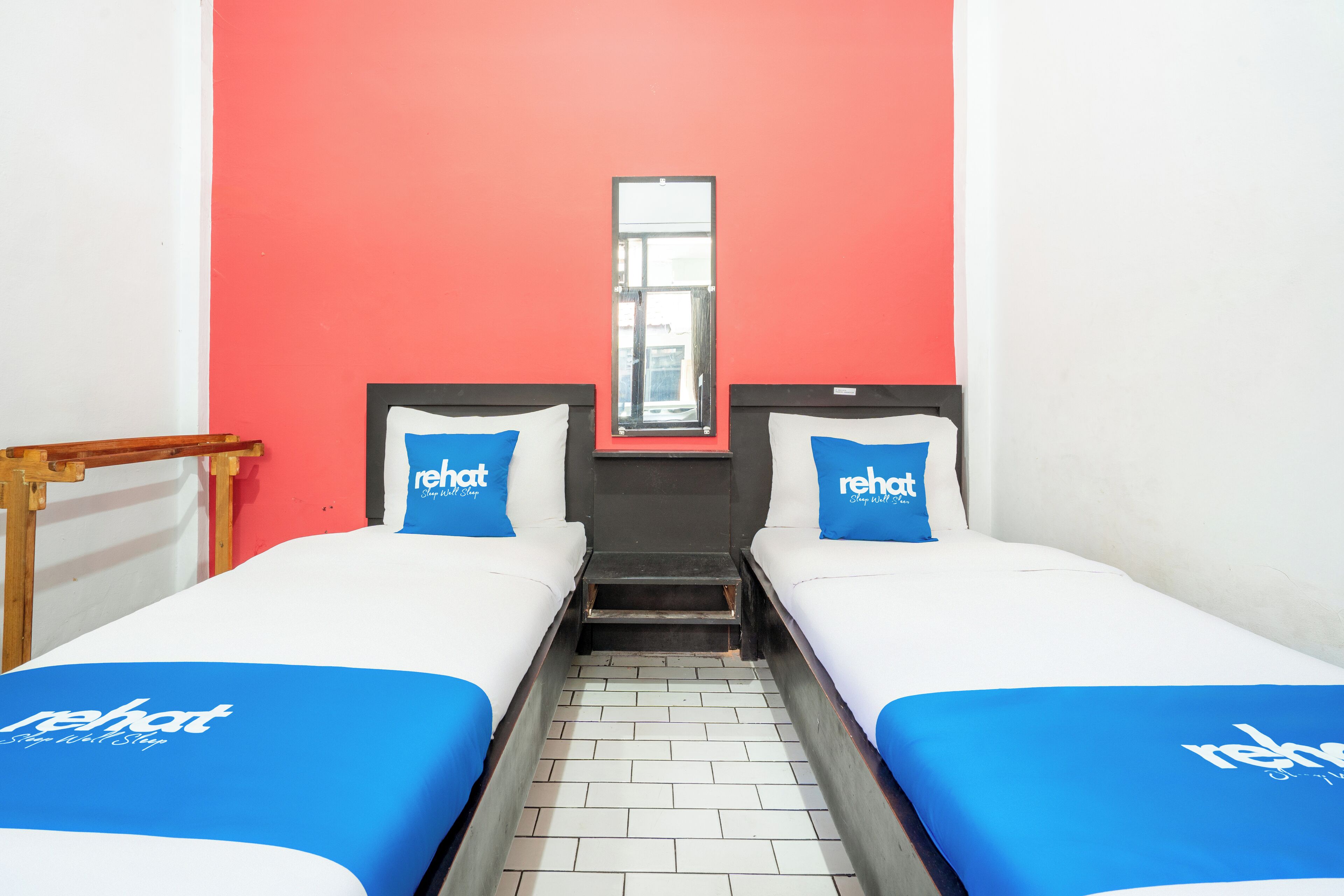 A hotel room with two beds, each with a blue bedspread and pillows, and a red accent wall.