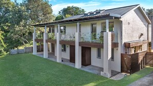Ein zweistöckiges Haus mit Balkon, umzäunter Garten und einer Holzterrasse.