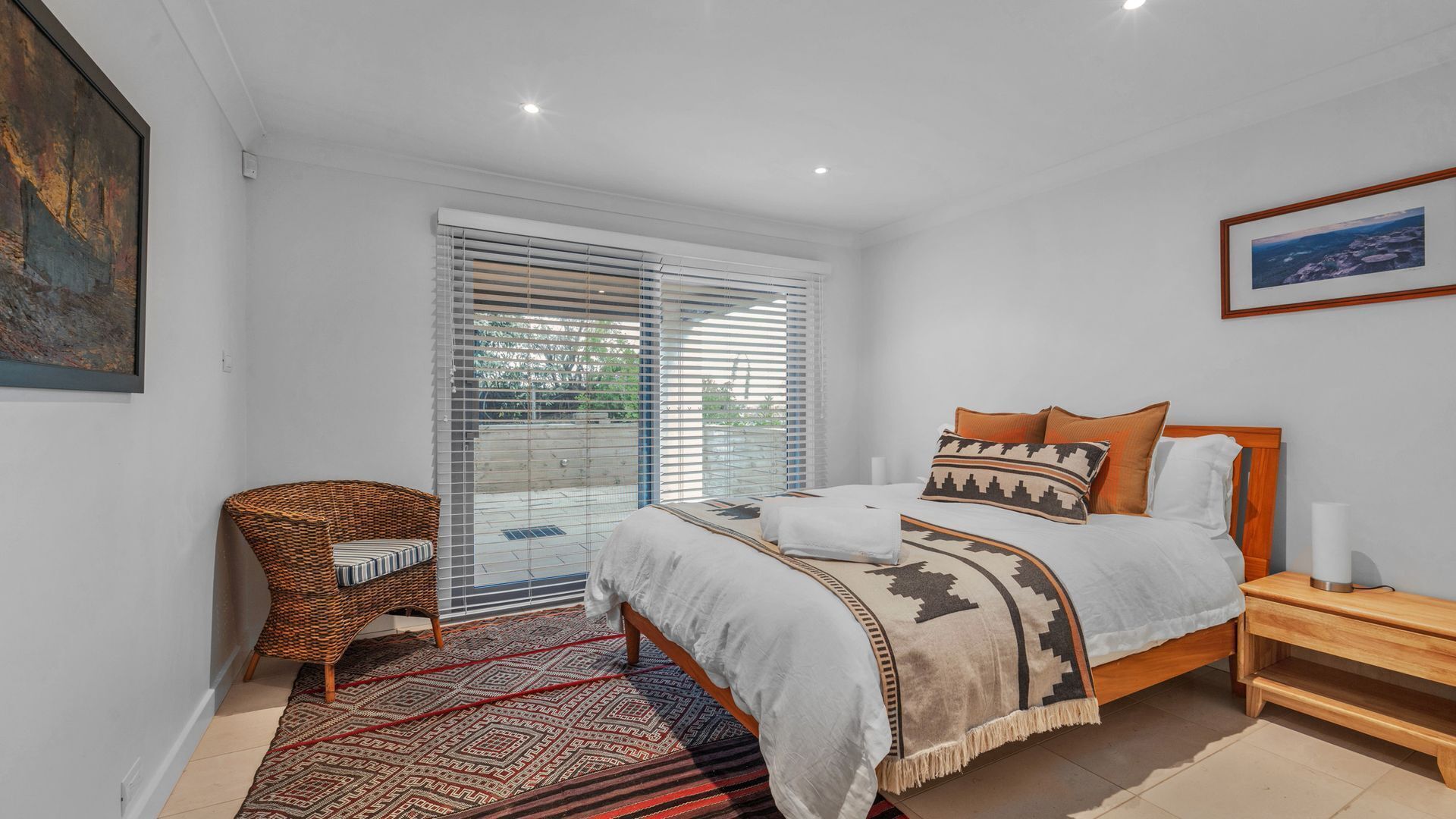 A bedroom with a bed, a chair, a bedside table, and a window with blinds.