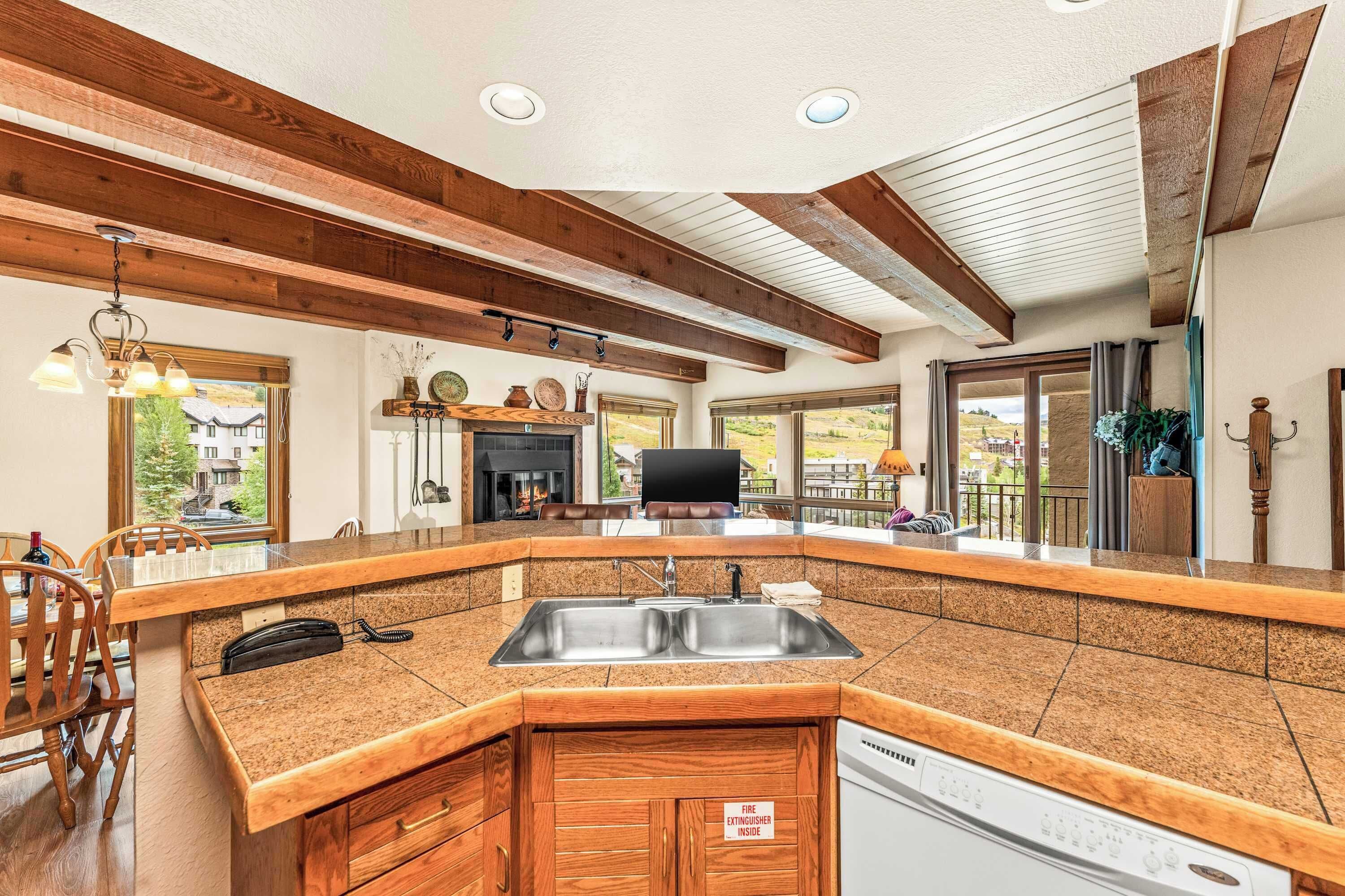 A kitchen with a granite countertop, wooden cabinets, a built-in dishwasher, and a fire extinguisher sign.