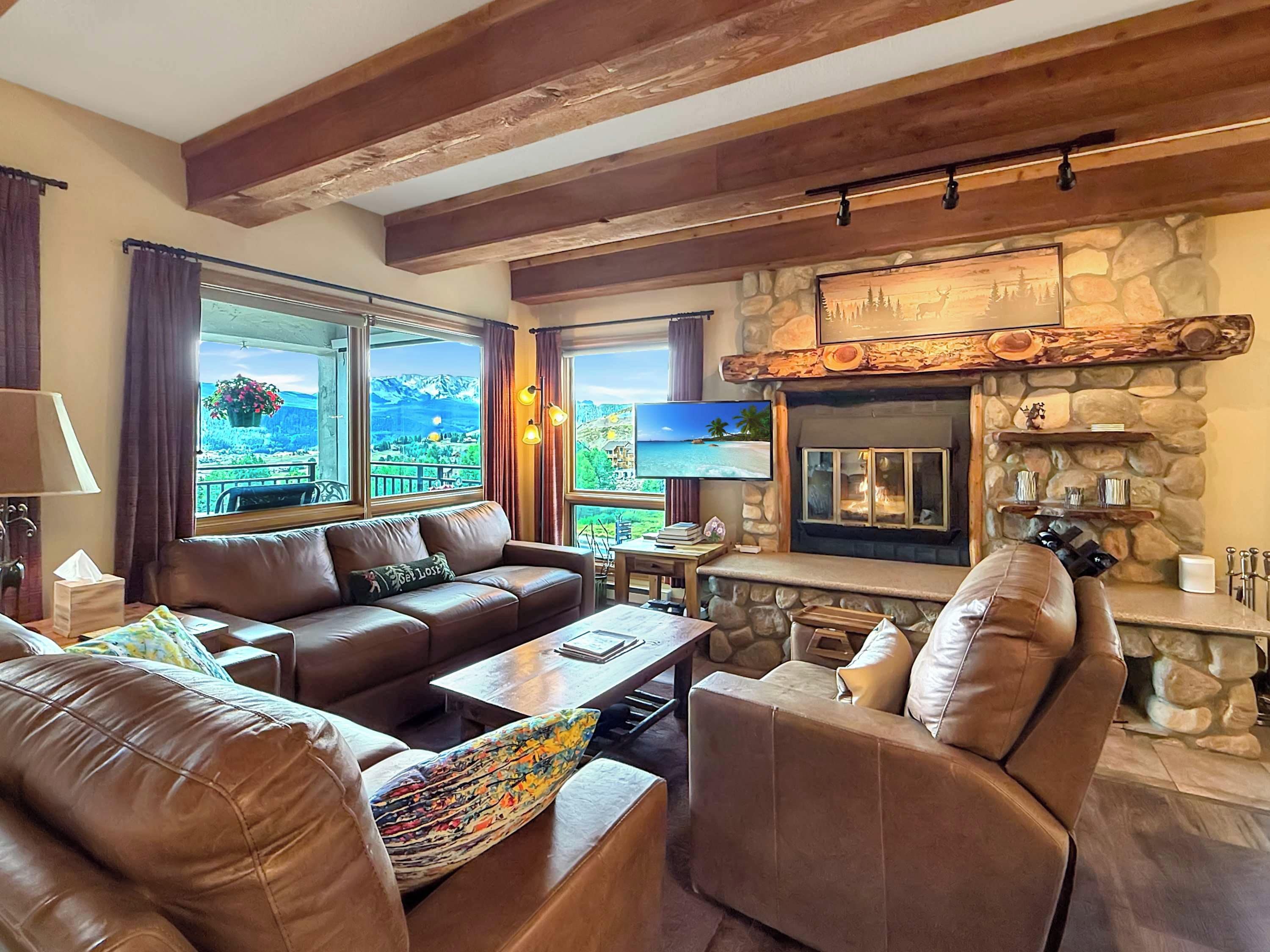 A cozy living room with a stone fireplace, leather sofas, and large windows offering scenic views.