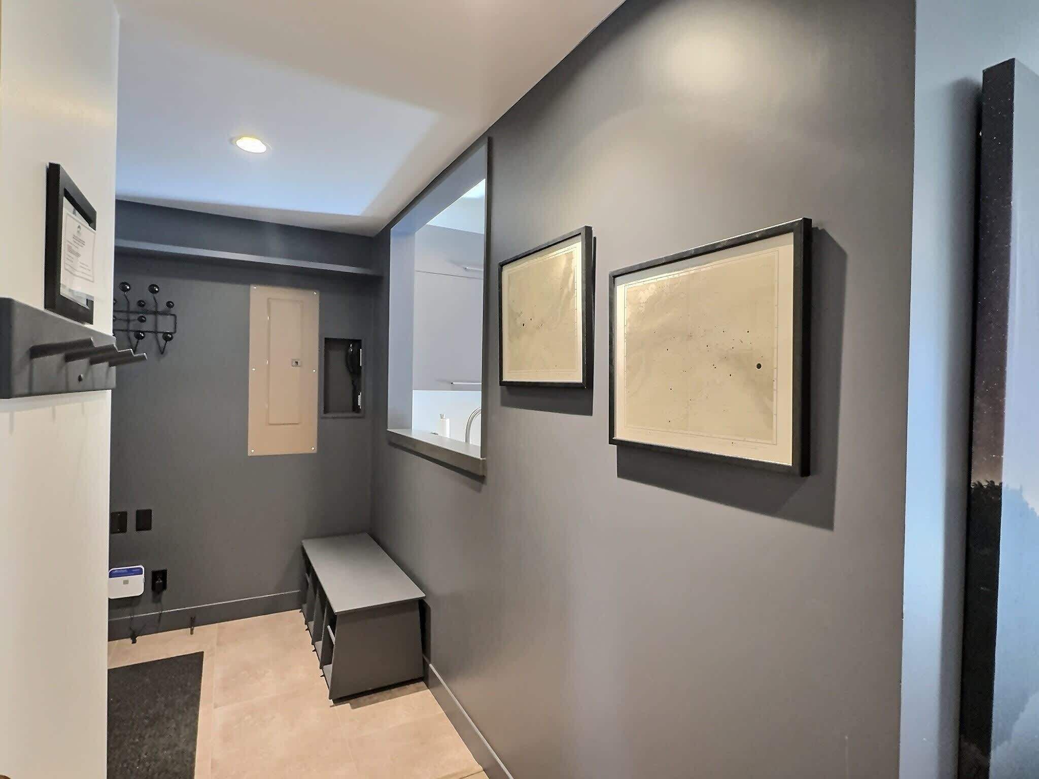 Une salle de bain moderne avec des murs gris, un banc, un miroir et des œuvres d’art encadrées.