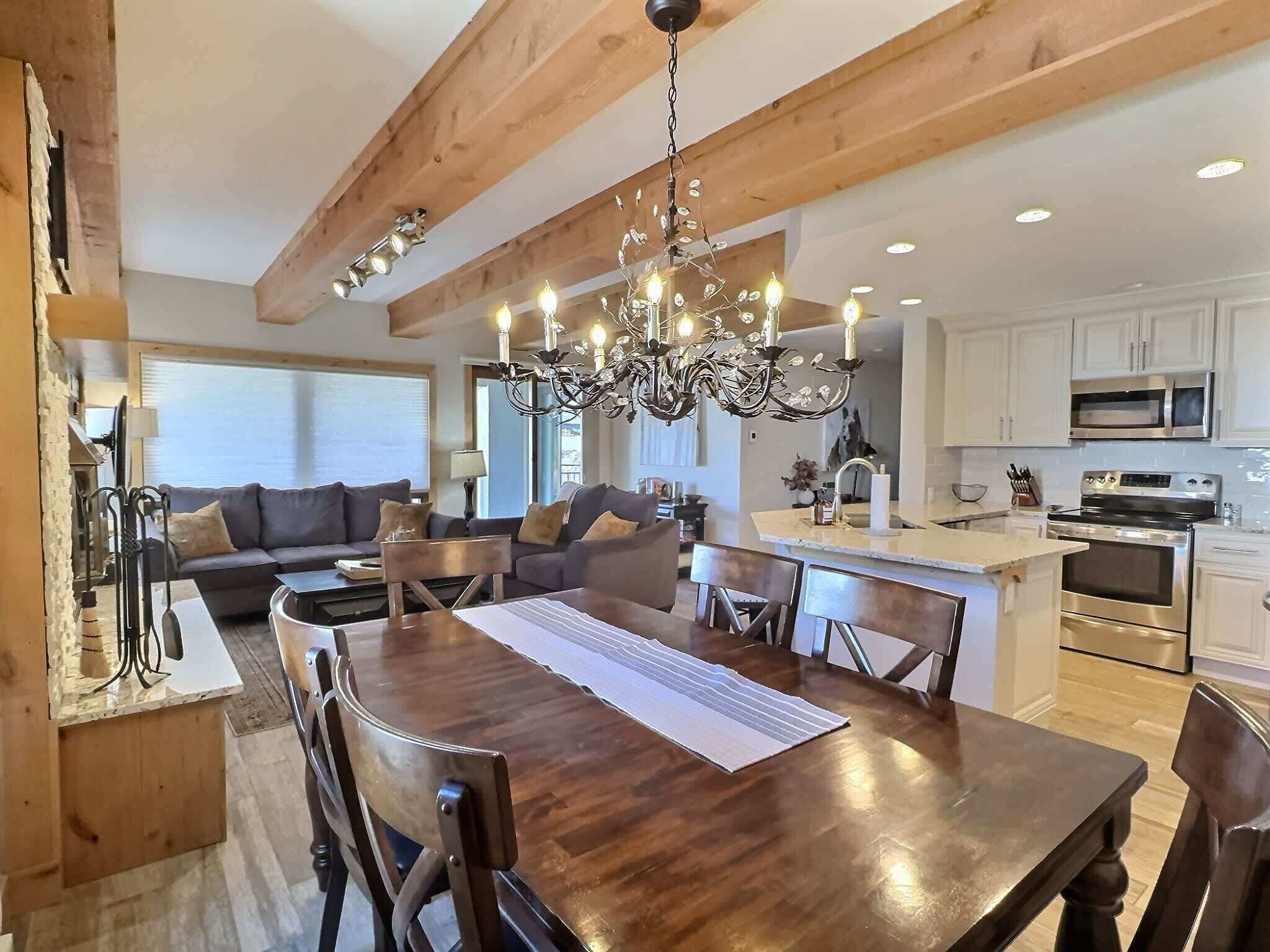 A modern kitchen with wooden beams, a chandelier, and a dining area with a wooden table and chairs.
