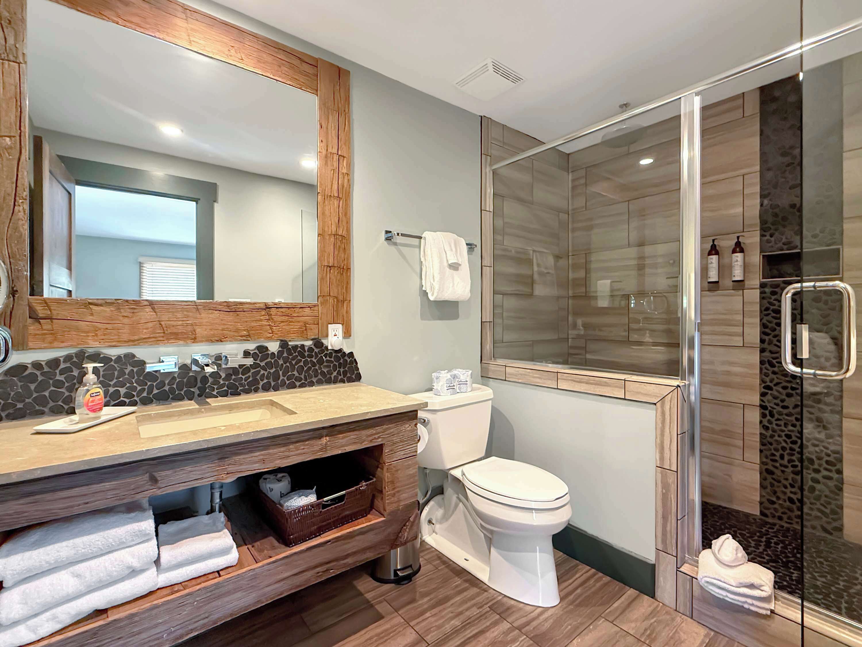 Un baño moderno con tocador de madera, inodoro, cabina de ducha de vidrio y un espejo grande.