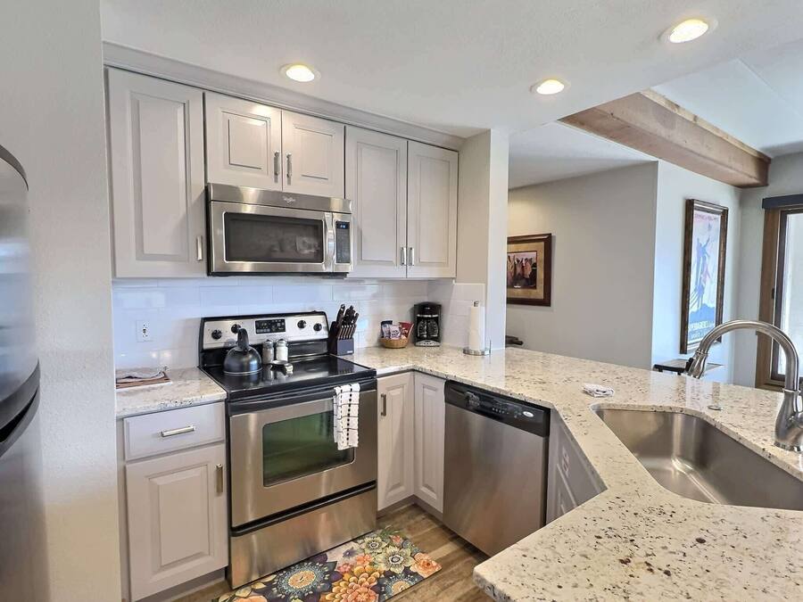 A modern kitchen with stainless steel appliances, white cabinetry, a granite countertop, and a built-in dishwasher.