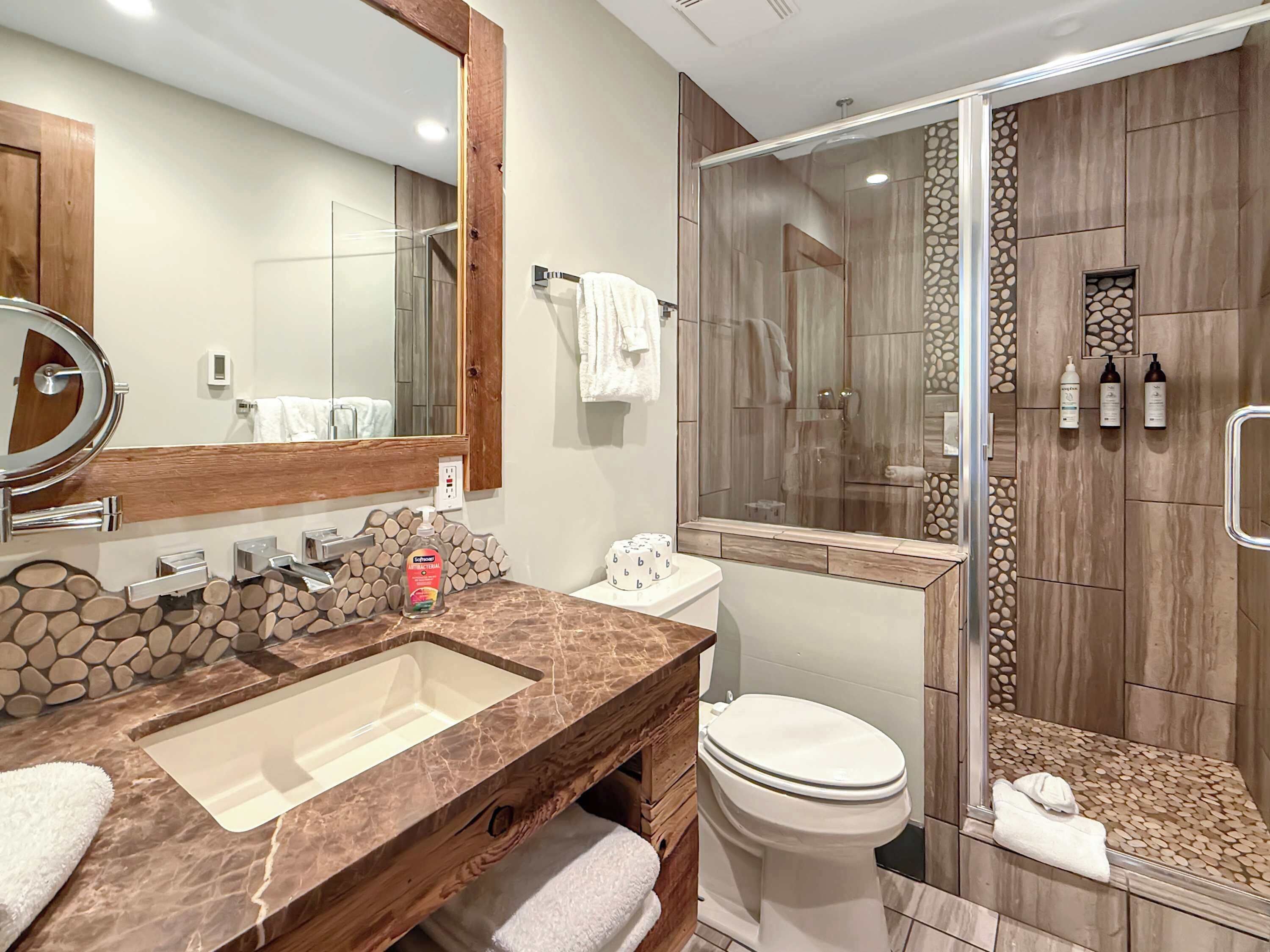 A bathroom with a marble sink, a toilet, a shower with a glass door, and a wooden vanity.
