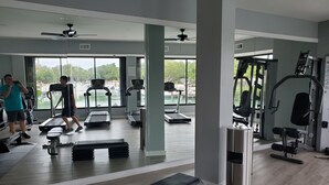 Ein Fitnessstudio mit Laufbändern, Crosstrainern und Gewichten. Große Fenster bieten Blick auf die grüne Umgebung.