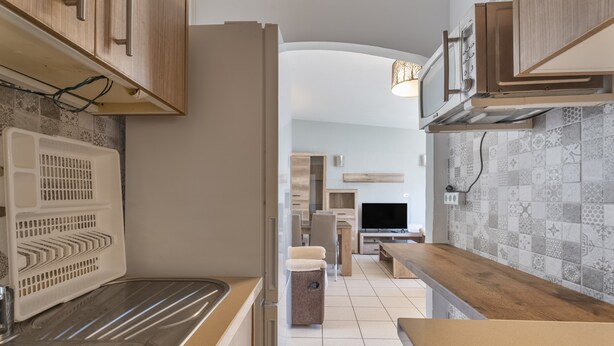 Een moderne keuken met een RVS-spoelbak, houten kastjes, een inbouwmagnetron en een decoratieve spatwand.