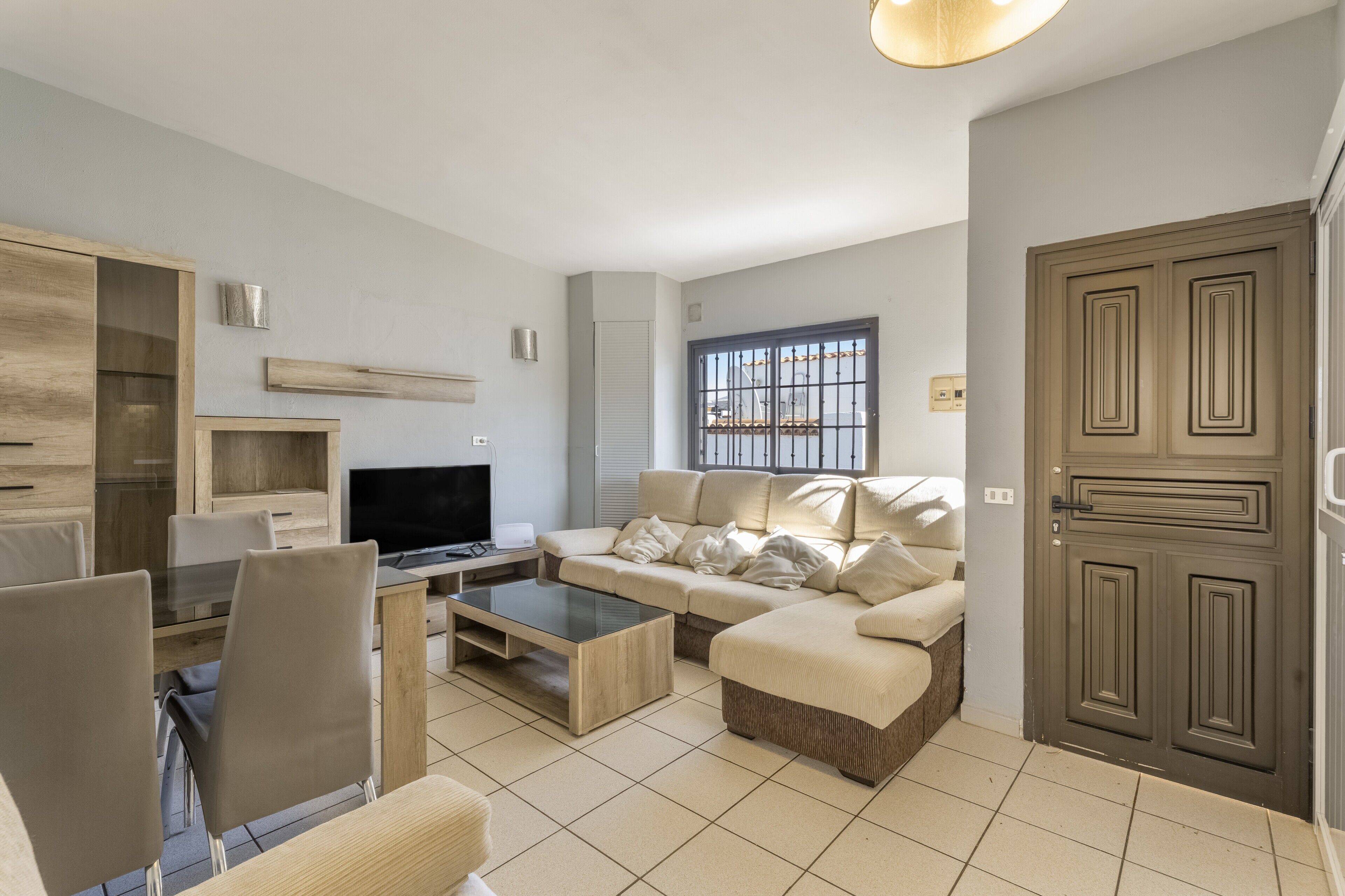 A modern living room with a sofa, coffee table, TV, and a dining area with chairs.