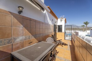 Eine Terrasse mit Tisch und Stühlen, eine Kachelwand und ein Tor zum Poolbereich.
