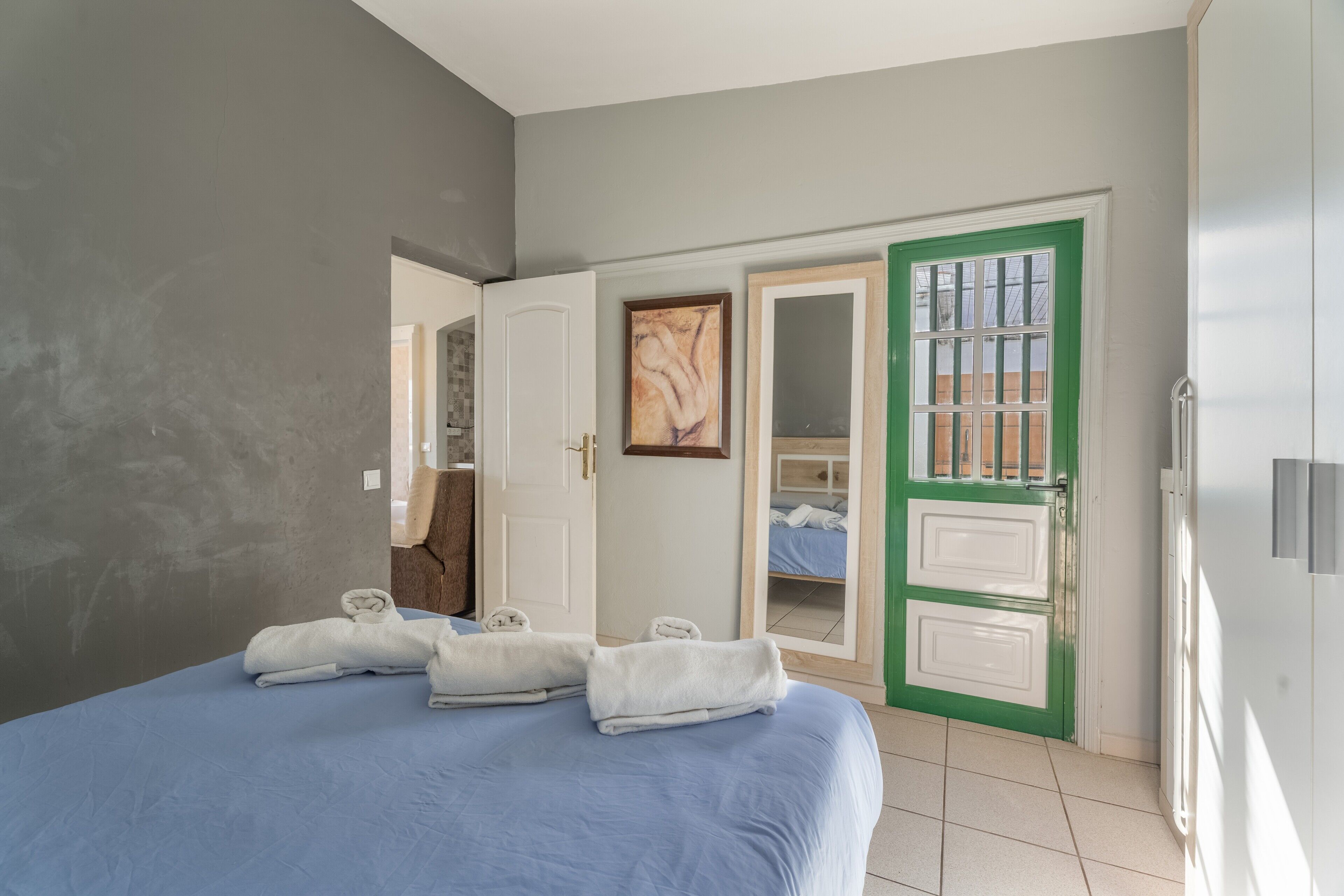 A bedroom with a bed, towels, a green door, and a painting.