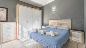 Een slaapkamer met een bed, een kledingkast, een nachtkastje en een wandlamp.