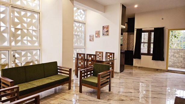 A spacious living area with a marble floor, a green sofa, wooden chairs, and a dining table. - Bricknest Hillview (Mysore)