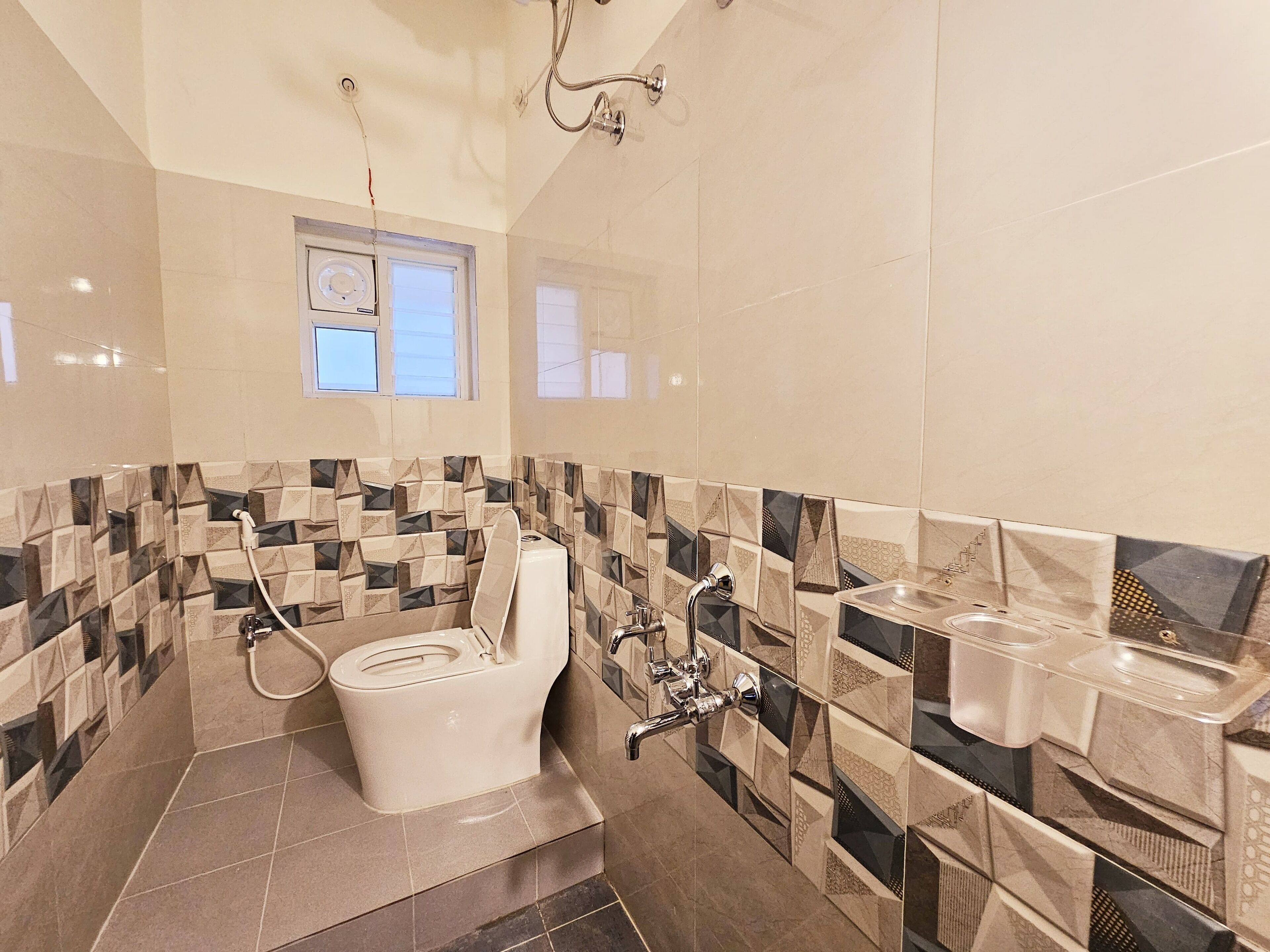 Bagno con WC, bidet e lavandino, con piastrelle a motivi geometrici e una finestra sopra il WC.