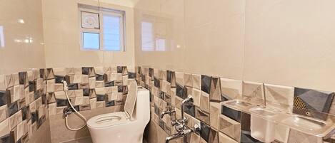 Bagno con WC, bidet e lavandino, con piastrelle a motivi geometrici e una finestra sopra il WC.