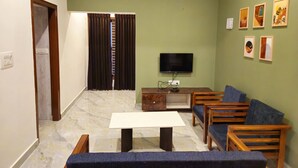 A living room with a TV, sofa, and table. - Bricknest Hillview (Mysore)
