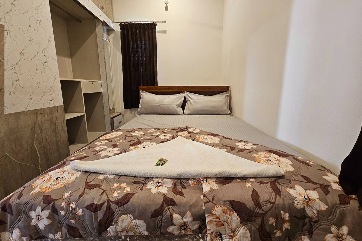Ein ordentlich gemachtes Bett mit einer blumigen Tagesdecke, einem Holz-Kopfteil und einem kleinen Nachttisch mit einer Lampe.