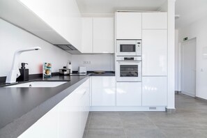 Una cucina moderna con mobili bianchi, un piano di lavoro nero, un forno a microonde Bosch e un forno.