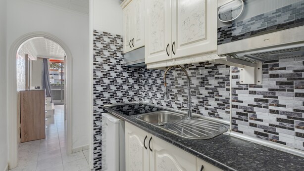 Una cocina con armarios blancos, encimera negra y salpicadero de azulejos.