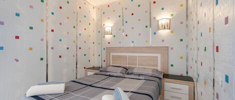 A neatly made bed with a checkered bedspread, two bedside tables with lamps, and a wall with colorful square patterns.