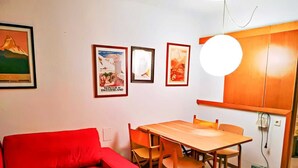 A compact living space with a red sofa, a wooden dining table with chairs, and a white cabinet with a light fixture above it. - Family Stay in Snowy Sierra Nevada (Monachil)