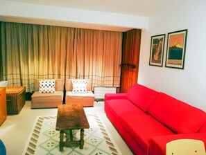 Un salon avec un canapé rouge, deux fauteuils, une petite table en bois et un tapis à motifs.