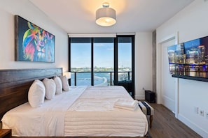 A bedroom with a large bed, a cityscape TV, and a view of the water. - Lux 2BD Apt: Stunning Water Views (Miami)