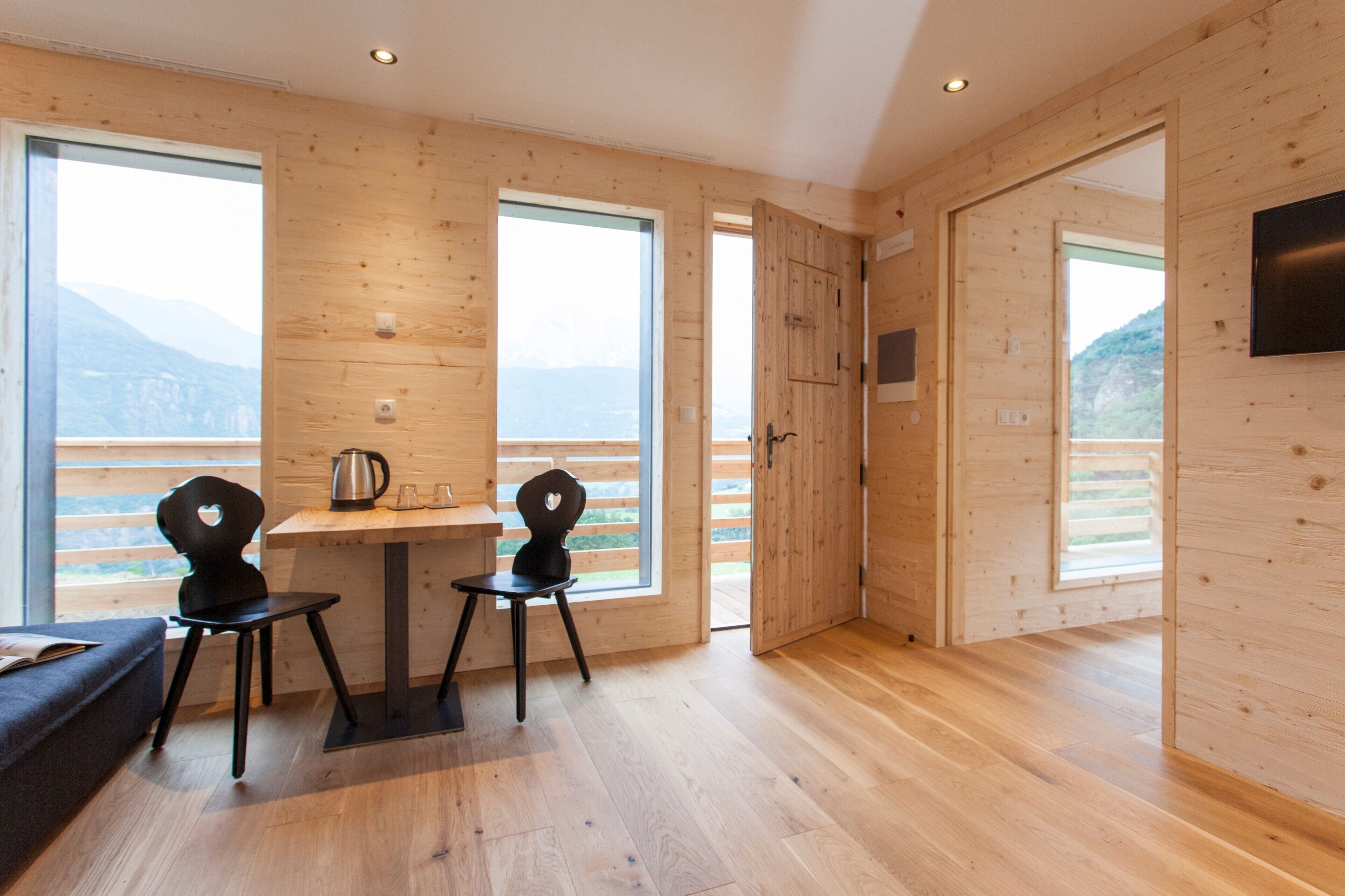 A wooden interior with a dining area, two chairs, a table, and a TV mounted on the wall.