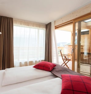 Hotellihuone, jossa on sänky, punainen tyyny, puinen tuoli ja parveke, jolta on näkymä.