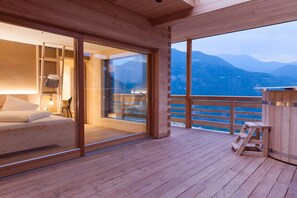 En træterrasse med en seng og en glasdør, der fører ud til en balkon med udsigt til et bjerglandskab.