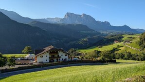 Ein Hotel mit Blick auf die Berge, mit weißer Fassade, Balkon und Parkplatz.