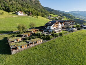 Ein modernes Resort mit mehreren Gebäuden, darunter ein großes Logis mit Balkon, in einem üppigen, grünen Tal mit Blick auf die Berge.