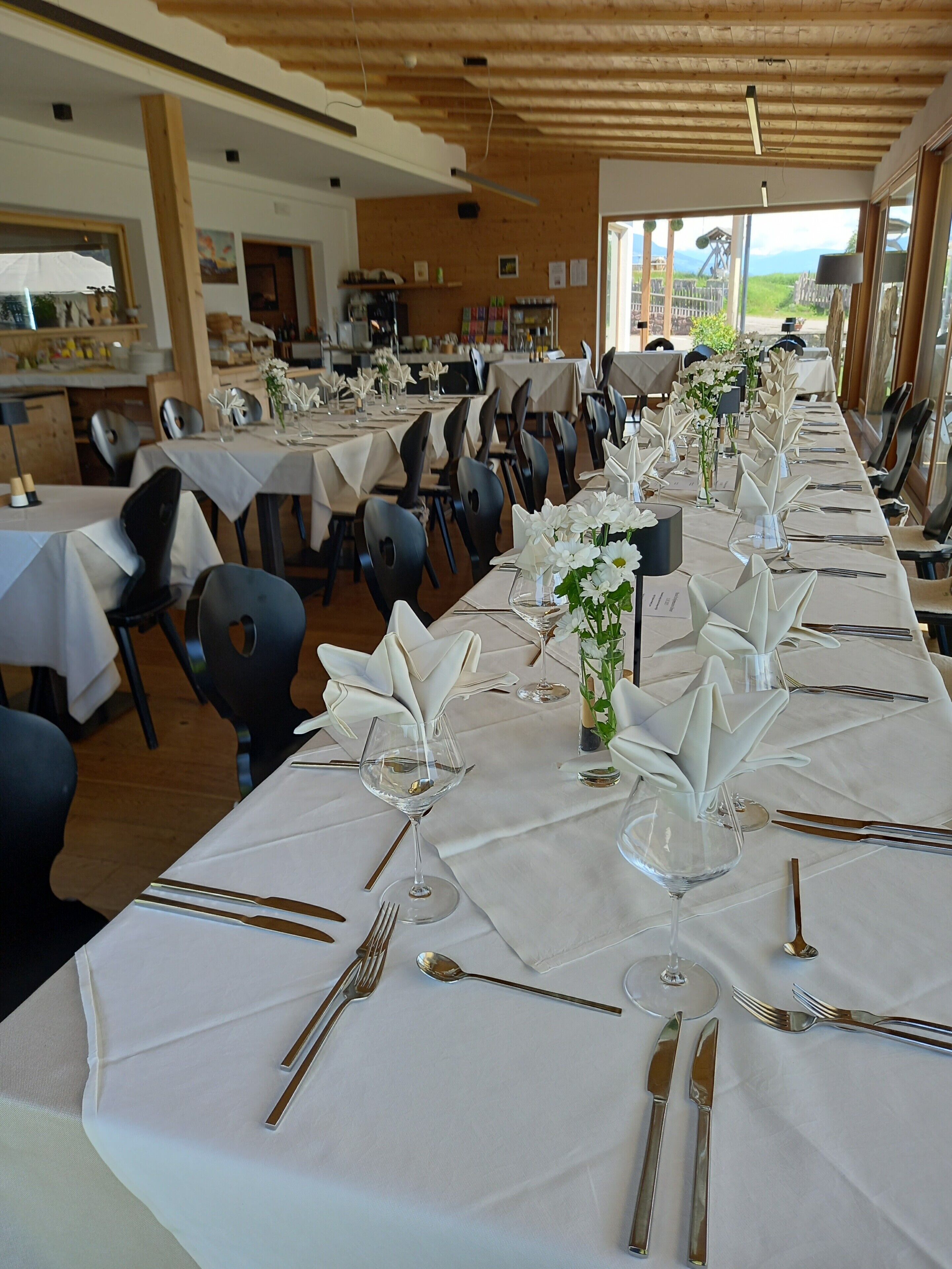 Een lange eettafel gedekt voor een formeel evenement, met witte tafelkleden, bestek en bloemstukken als decoratie.
