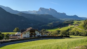 Hotel met uitzicht op de bergen, een witte gevel, een balkon en een parkeerplaats.