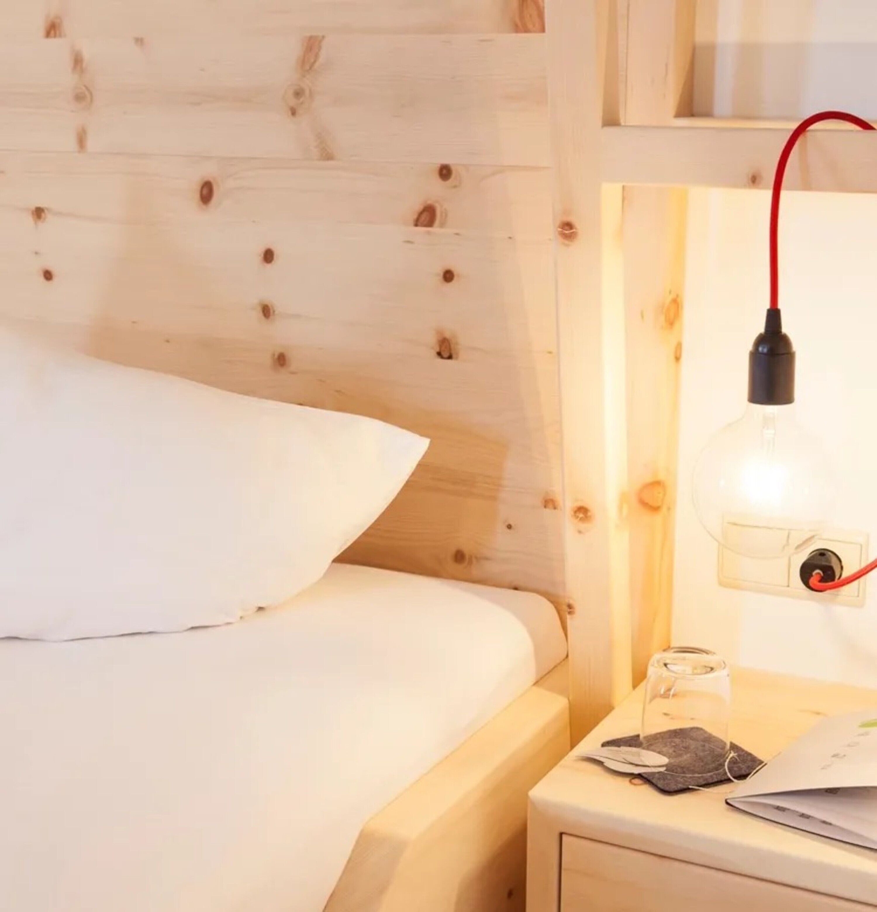 Cabecera de madera, lámpara de noche, mesita de noche con un vaso y un ordenador portátil.