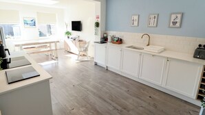 A modern kitchen with white cabinets, a sink, and a countertop. There is a dining area with a bench and chairs. - The Seaside Retreat (Mablethorpe)