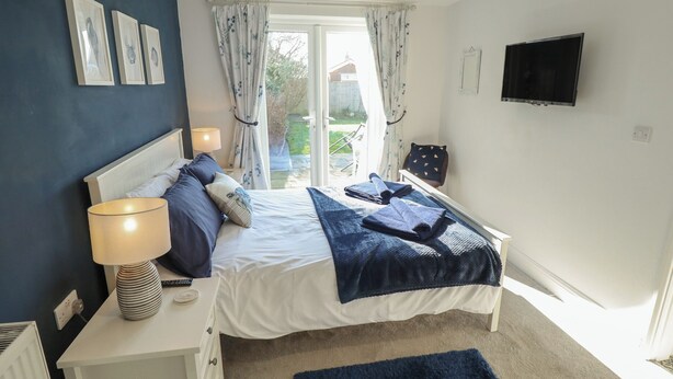 A bedroom with a bed, bedside lamp, TV, and a view of the outdoors. - The Seaside Retreat (Mablethorpe)