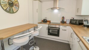 Une cuisine moderne avec des meubles blancs, un four en acier inoxydable, un four à micro-ondes et une grande horloge décorative.