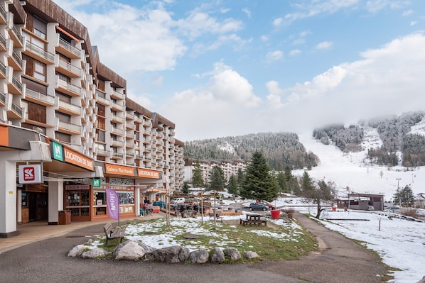 Un hôtel à plusieurs étages doté de balcons, d’un magasin de ski et offrant une vue sur une montagne enneigée.