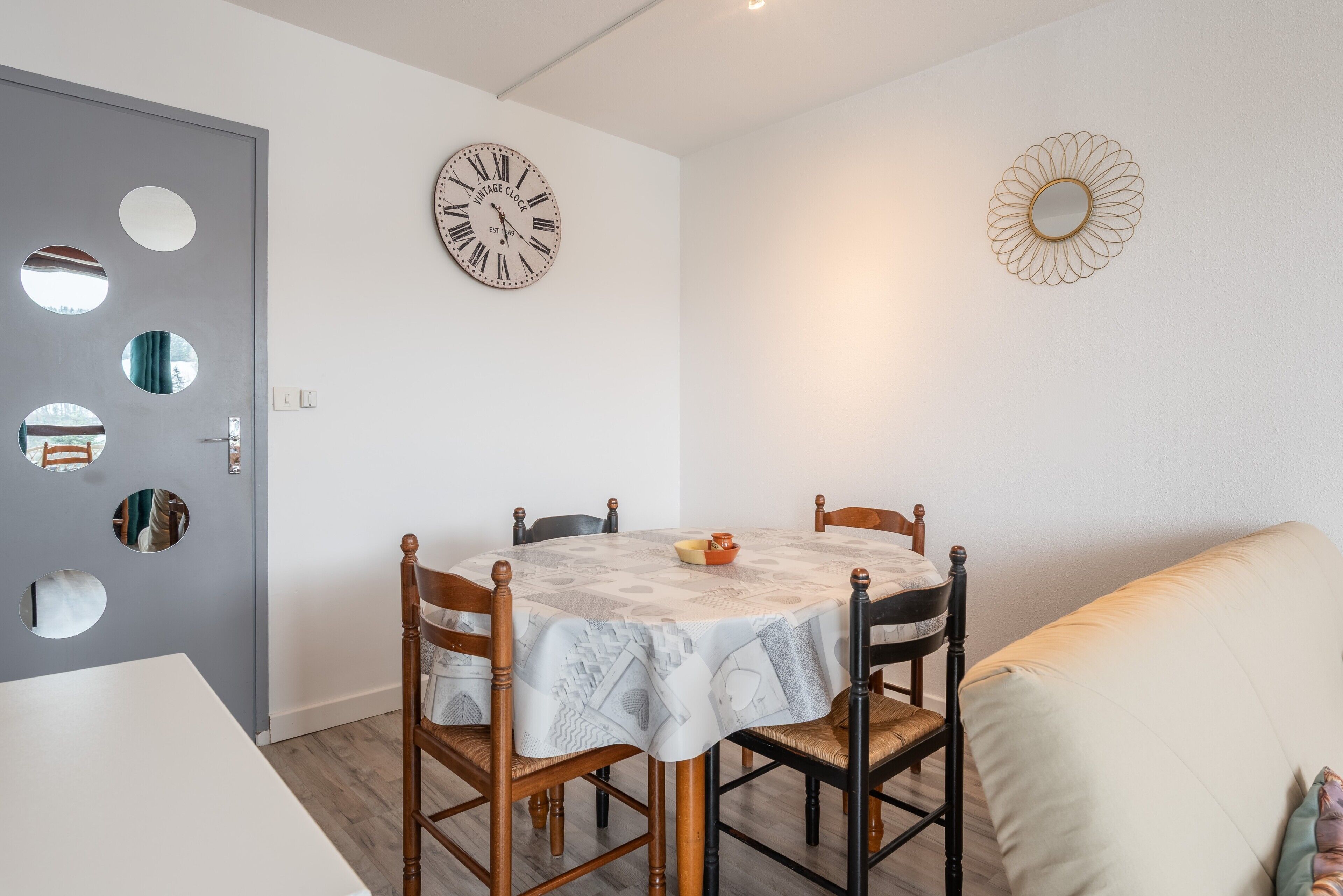 Un comedor con una mesa redonda, cuatro sillas, un reloj y un espejo en la pared.