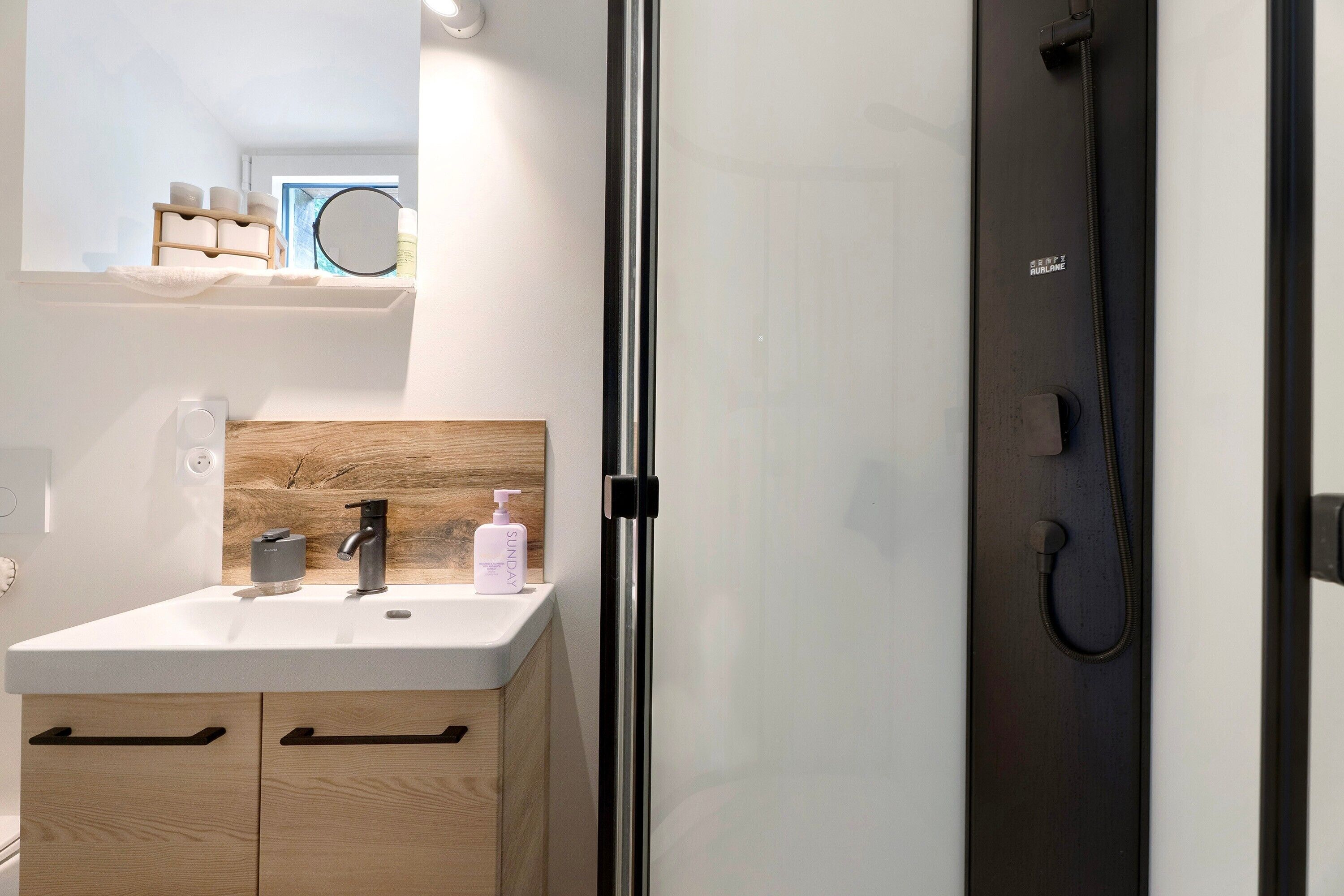 Une salle de bain moderne avec un lavabo blanc, un meuble-lavabo en bois, un miroir et une douche.